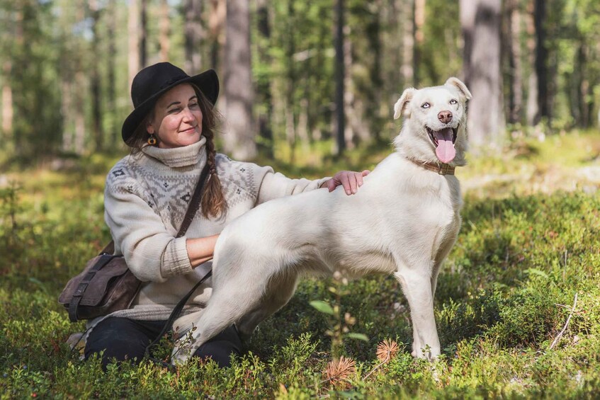 En person sitter på marken tillsammans med en stor, vit hund i ett skogsområde. 2