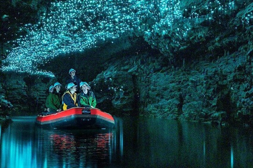 A group of people in a raft navigating a cave with bioluminescent organisms. 5