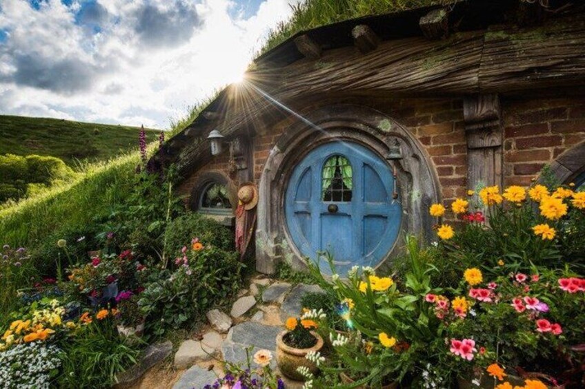 A Hobbit-style house with a blue door, surrounded by colorful flowers and greenery. 1