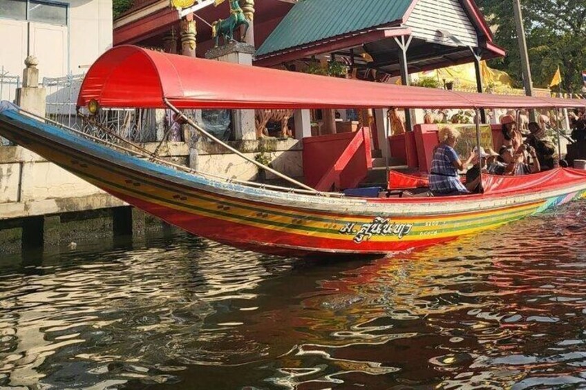 A colorful boat with passengers, a red canopy, and a building with a green roof in the background. 4