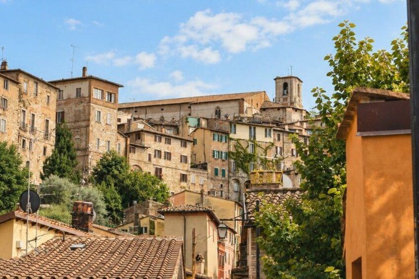 A historic town with terracotta-roofed buildings, a bell tower, and lush greenery. 2