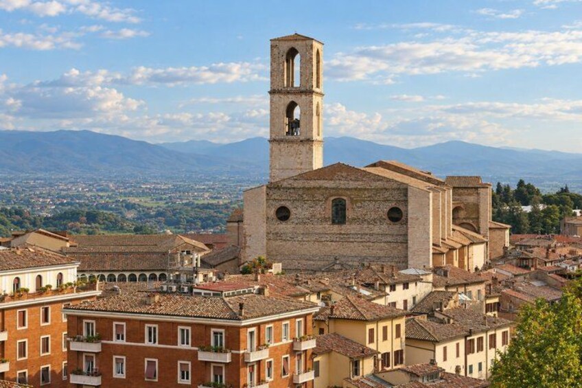 A historic town with a prominent church featuring a bell tower, surrounded by traditional buildings and a mountainous backdrop. 3
