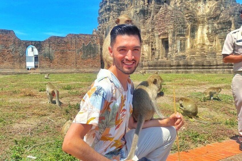 A man with a monkey on his shoulder, a temple in the background, and another monkey on the ground. 4