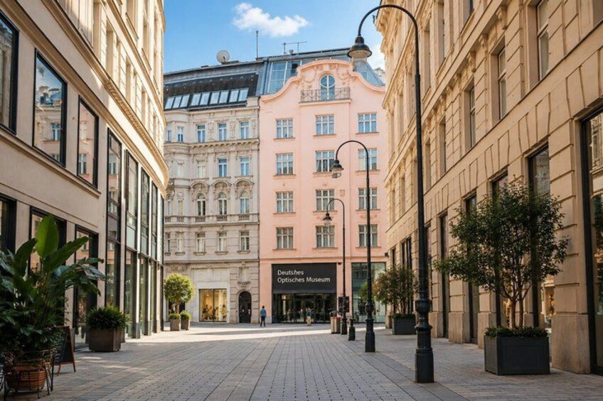 A city street with buildings, a Deutzisches Museum sign, and potted plants. 2