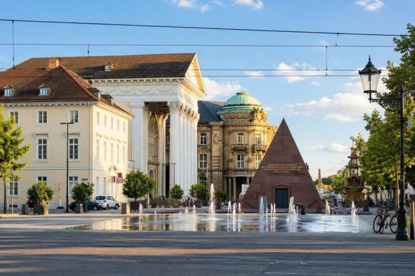 A historic square with classical architecture, a prominent obelisk, and a fountain. 5