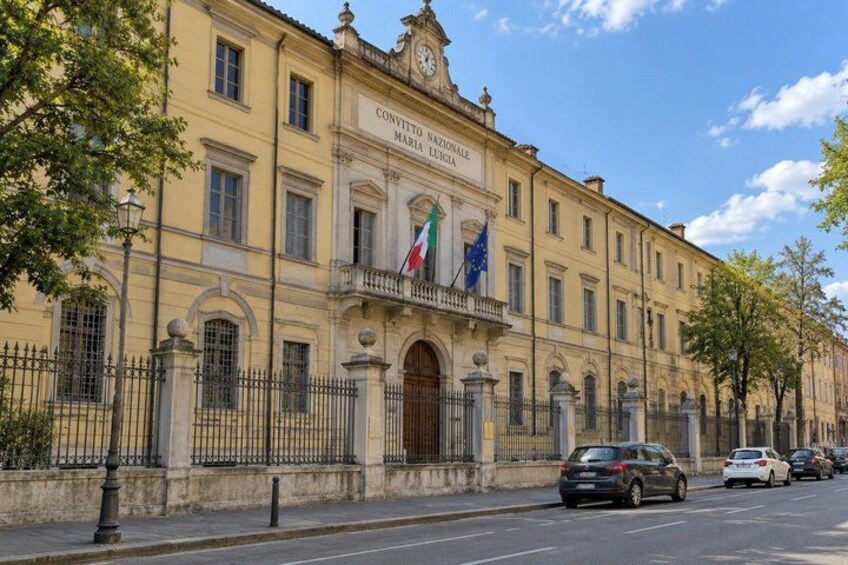A historic building with a clock tower, flags, and a street in front. 4
