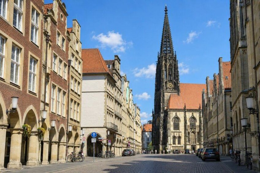 A cobblestone street lined with historic buildings, a prominent church spire, and bicycles parked along the sidewalk. 3
