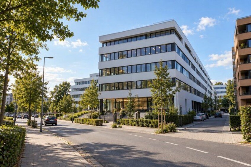 A modern multi-story building with a flat roof, surrounded by trees and a clear sky. 4