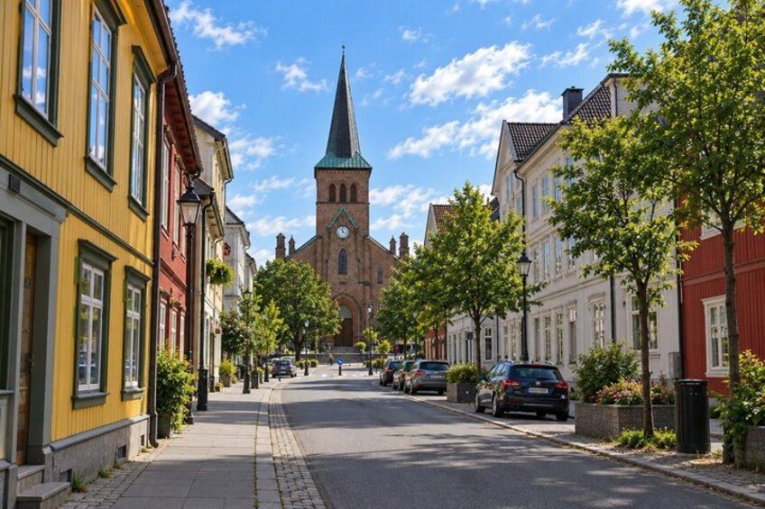 A street with buildings, a church tower, and parked cars. 3