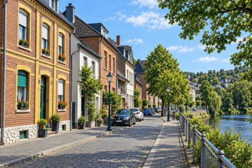 A cobblestone street lined with historic buildings, a river, and parked cars. 2