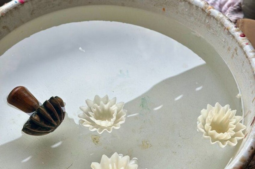 A ceramic bowl with a wooden handle, containing three white ceramic flowers. 2