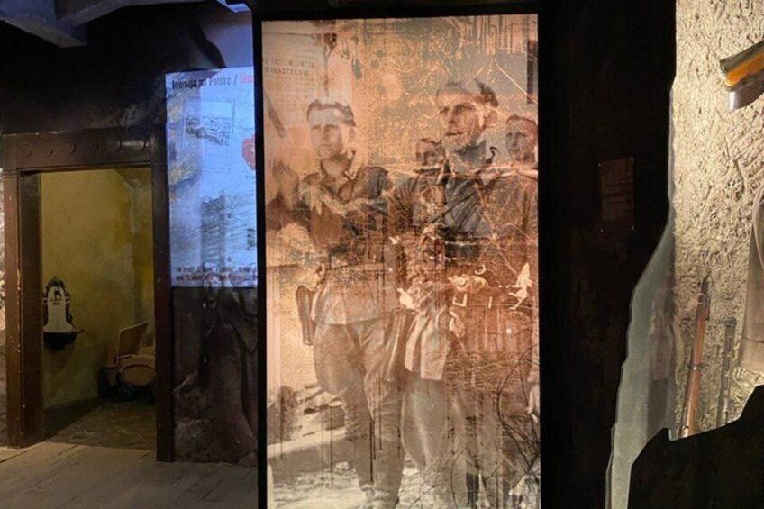 A historical exhibit with a large poster featuring soldiers, a wooden door, and a stone wall. 3