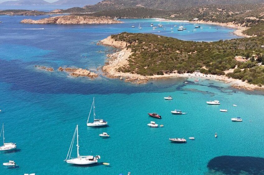 A coastal area with clear turquoise waters, several boats, and rocky terrain with sparse vegetation. 3