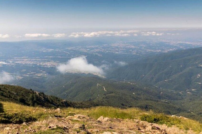 A mountainous landscape with a winding road, dense forest, and a distant cityscape. 2