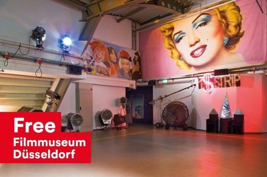 An indoor space with a large mural, industrial lighting, and a red banner advertising a free film museum. 4