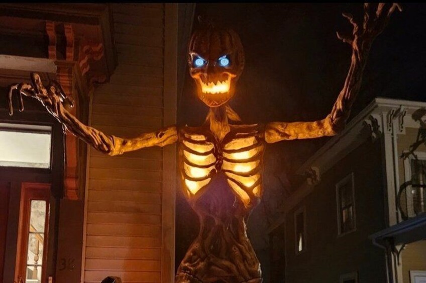 A skeleton figure with glowing eyes and arms extended, standing in front of a house. 2