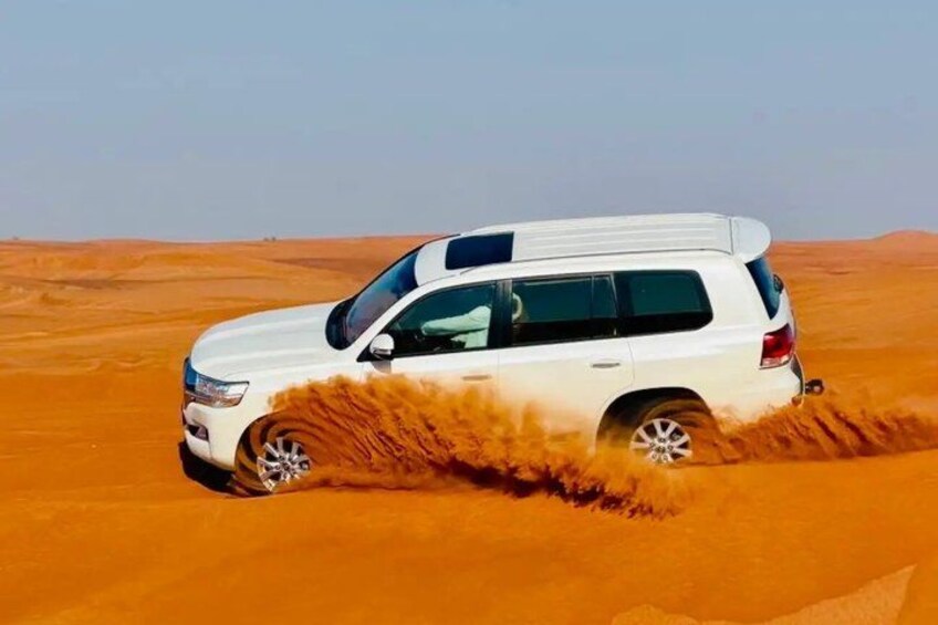 A white SUV driving through a desert with sand being kicked up behind it. 1