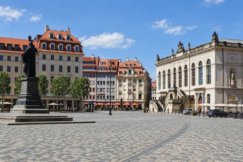A cobblestone square with a statue, historic buildings, and a clear sky. 3