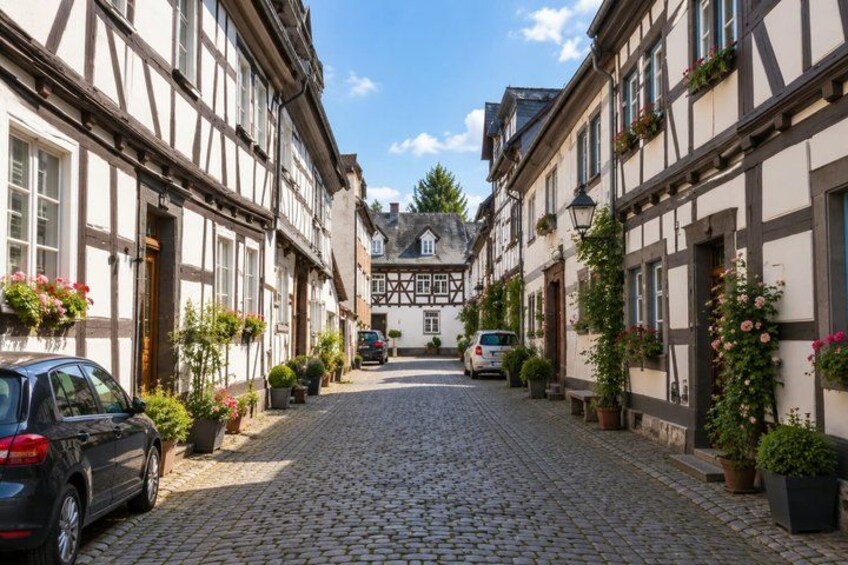 A cobblestone street lined with traditional half-timbered houses, parked cars, and potted plants. 4