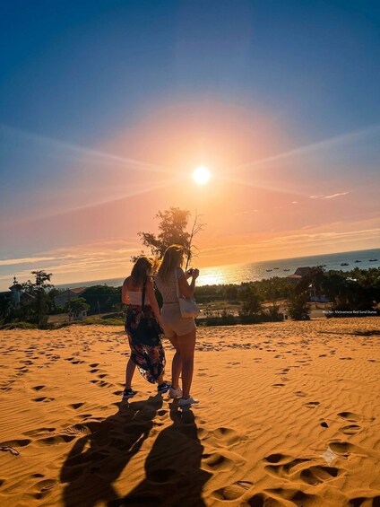 Two people standing on a sandy beach with the sun setting in the background. 3