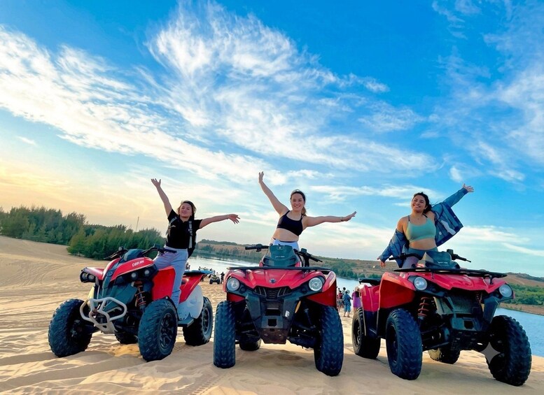 Three people on ATVs on a sandy beach with a lake and trees in the background. 4
