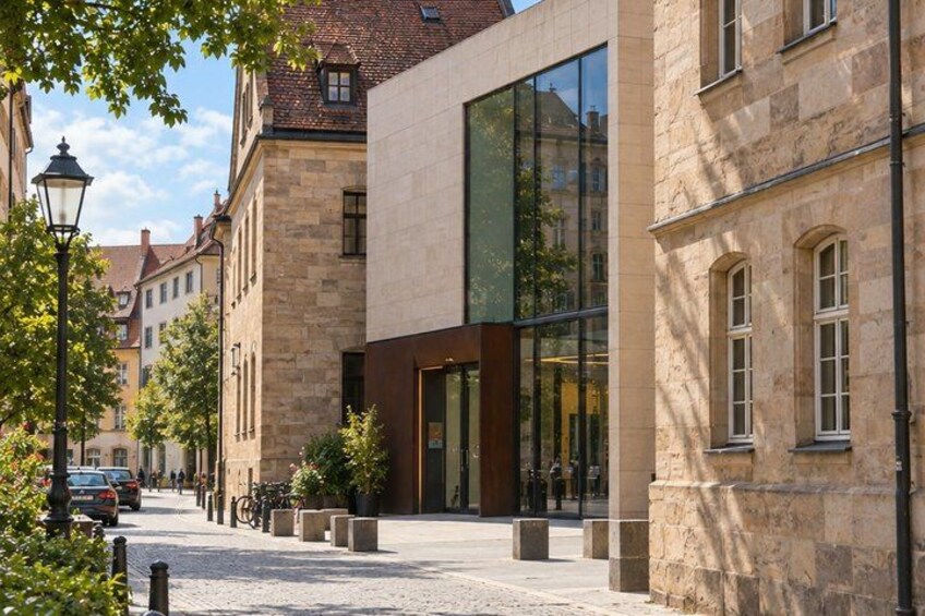 A cobblestone street lined with historic buildings, a modern glass building, and a lamppost. 3