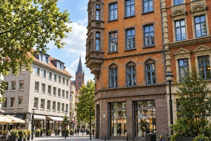 A street with buildings, trees, and a church spire in the background. 2