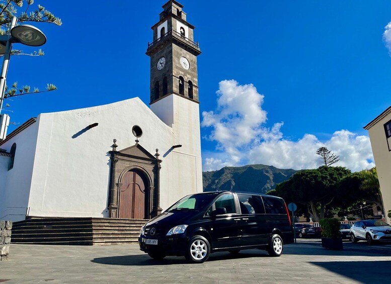 Une voiture noire est garée devant une église blanche dotée d’un clocher, sous un ciel bleu dégagé. 3