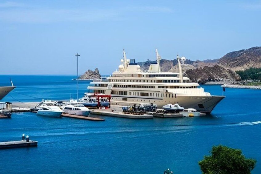 A large cruise ship docked at a marina with smaller boats nearby, surrounded by clear blue water and a hilly landscape in the background. 4
