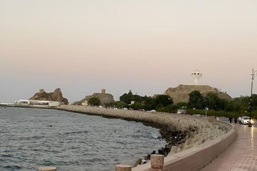 A waterfront promenade with a stone barrier, a lighthouse, and rocky formations in the background. 3