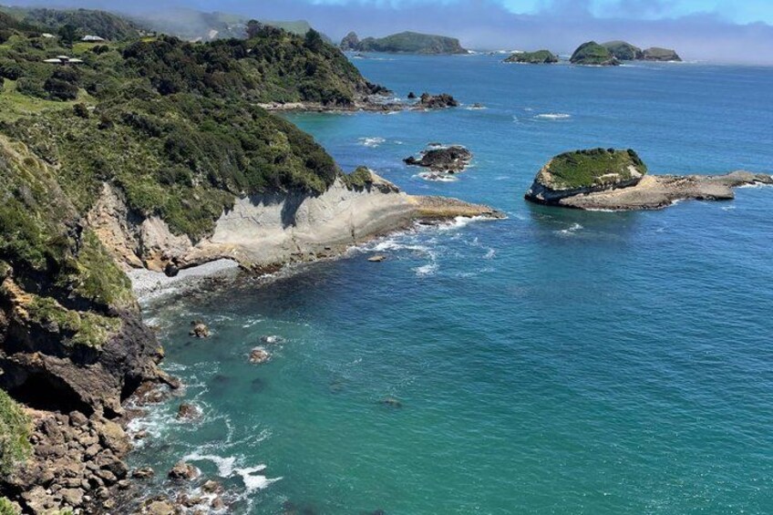 A coastal landscape with rocky cliffs, clear turquoise waters, and small islands. 3
