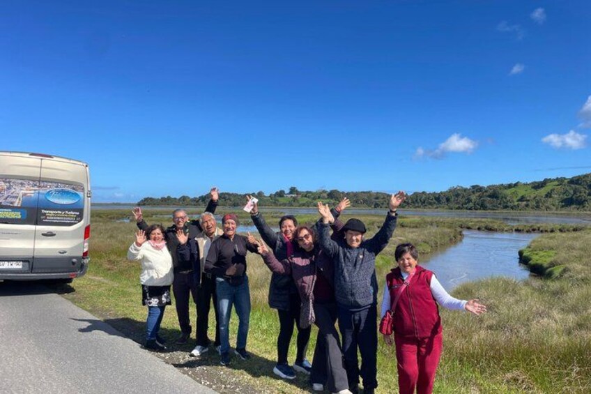 A group of people standing by a road with a river and greenery in the background. 2