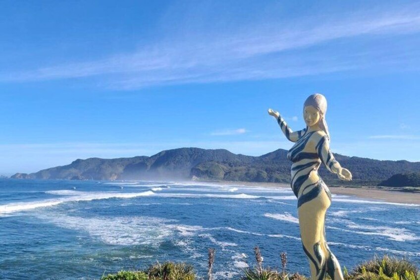 A statue of a woman in a swimsuit by the ocean with waves and mountains in the background. 5