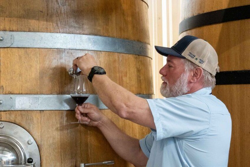 A person pouring wine from a barrel into a glass. 5