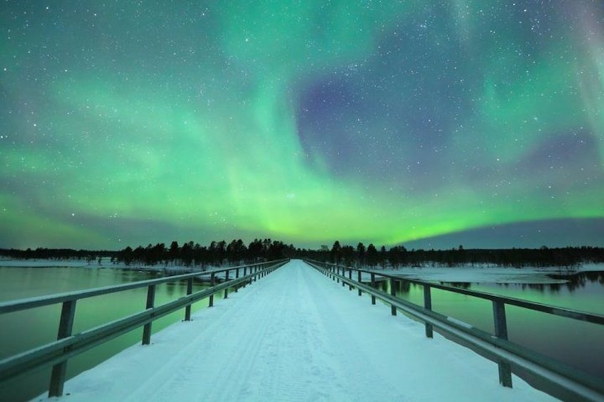 A snowy road with a railing, under a night sky with the aurora borealis. 1