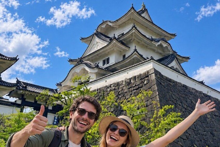 A traditional Japanese castle with multiple tiers and a stone base, surrounded by greenery. 1