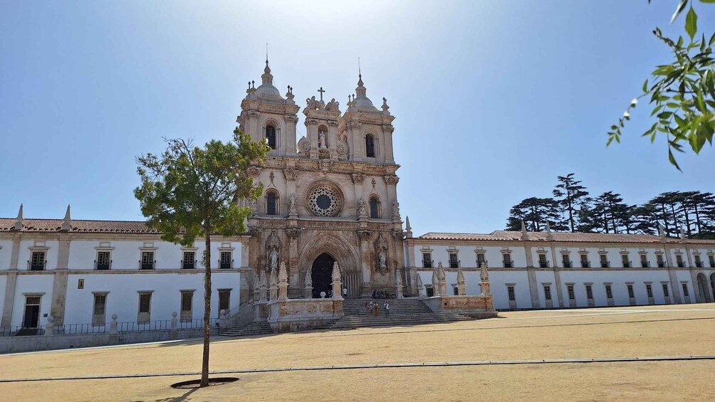 Una catedral histórica con una alta torre de reloj, rodeada por un patio con un árbol y un edificio con tejado de baldosas. 4