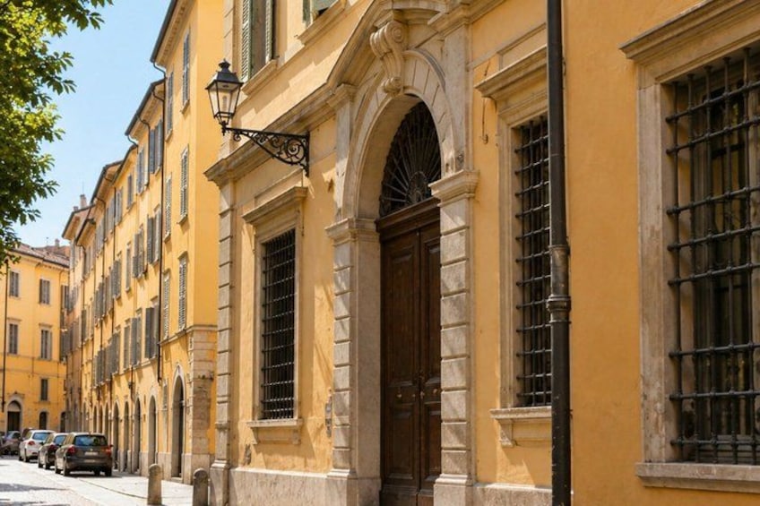 A yellow building with a large wooden door, arched windows, and a street with parked cars. 5