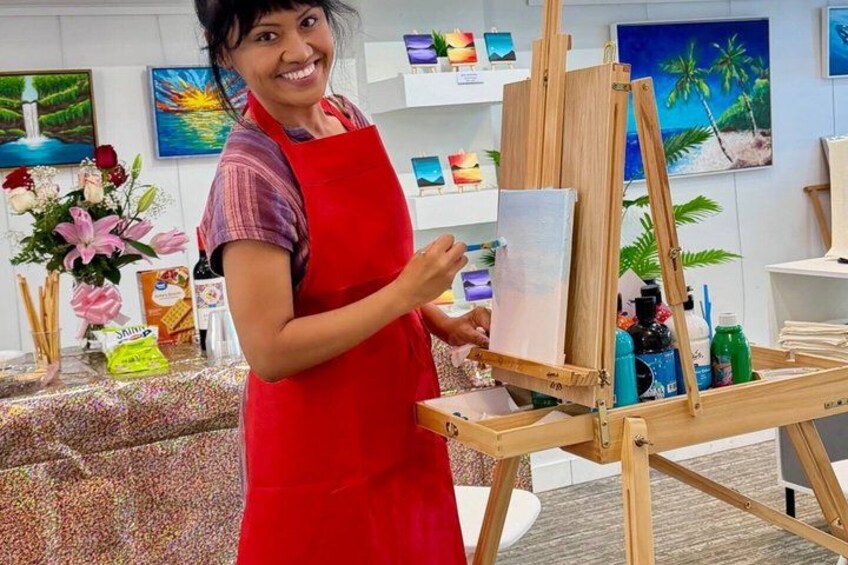 A person painting on a wooden easel in a room with art supplies and paintings on the walls. 5