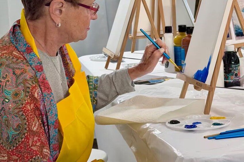 An individual painting on an easel with a palette of colors. 1
