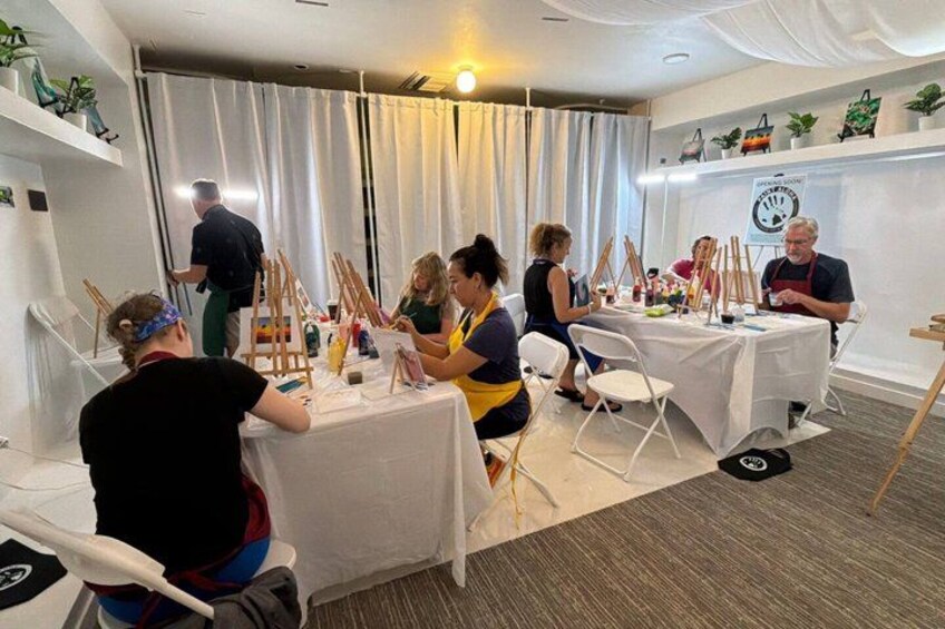 A group of people engaged in a painting activity, with easels and paint supplies on tables. 3