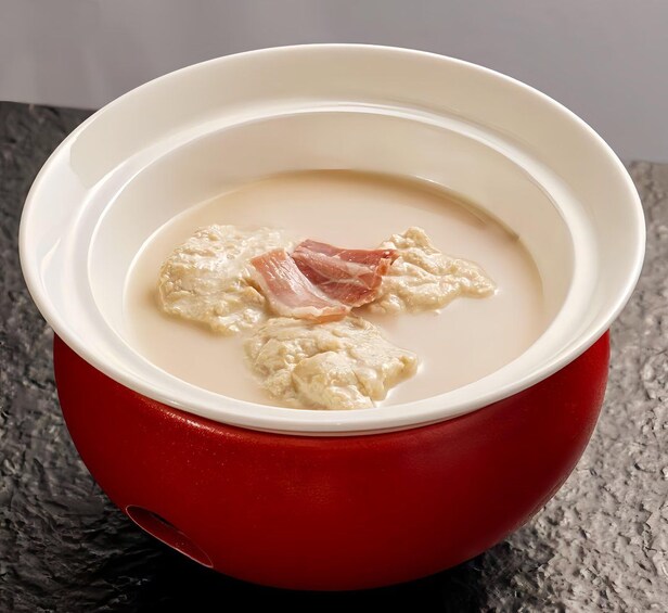 Un bol de soupe, de couleur rouge à l’extérieur et blanche à l’intérieur, contenant un morceau de viande et une substance crémeuse. 4