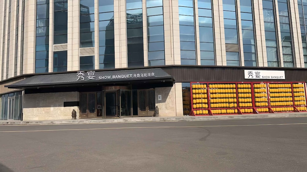 Un bâtiment sur lequel est apposée une enseigne indiquant « SALLE DE SPECTACLE ET BANQUET », et devant lequel est alignée une rangée de chaises jaunes. 3