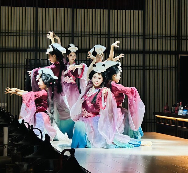 Un groupe d’artistes, vêtus de costumes traditionnels, se produit sur une scène dont le décor est constitué de lignes verticales. 1