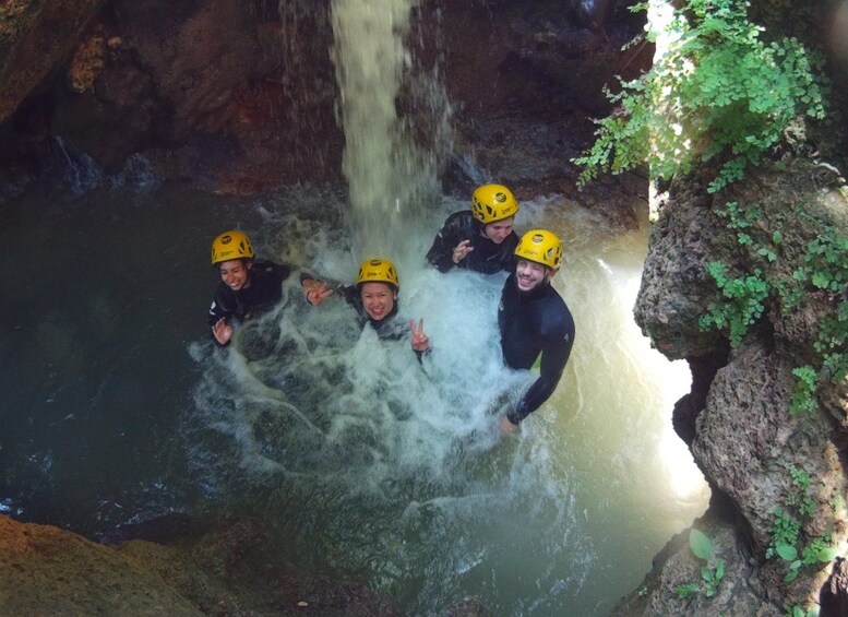 Un groupe de personnes, portant des casques et des combinaisons de plongée, se trouve dans une grotte remplie d’eau, où une cascade se déverse. 1