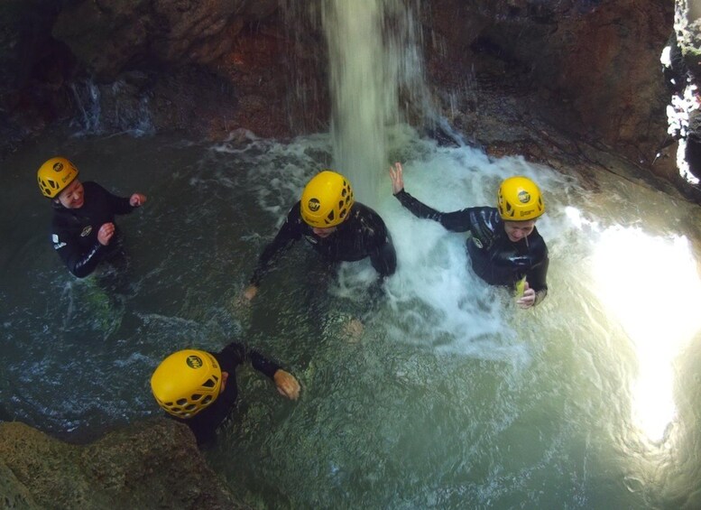 Quatre personnes, vêtues de combinaisons de plongée et portant des casques, se trouvent dans une grotte remplie d’eau, où une cascade se déverse. 3