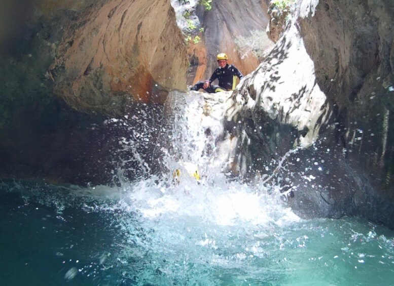 Une personne assise sur un rebord rocheux au-dessus d’une cascade, portant un casque et un gilet de sauvetage. 2