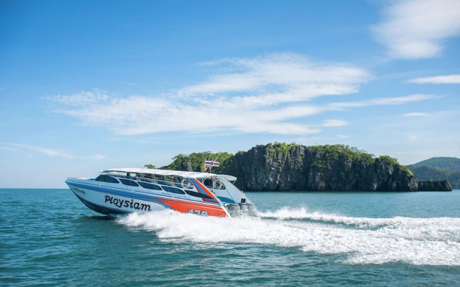 A speedboat with 'Ploysiam' written on the side, moving through calm waters with a rocky island in the background. 3