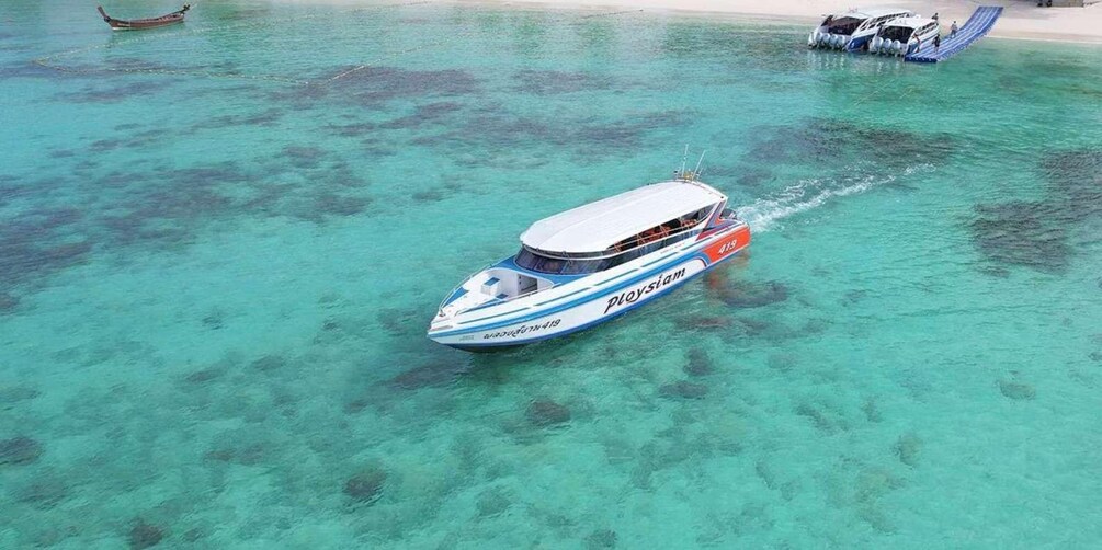 A speedboat named 'Ploysiam' on clear turquoise water with a sandy beach and another boat in the background. 4