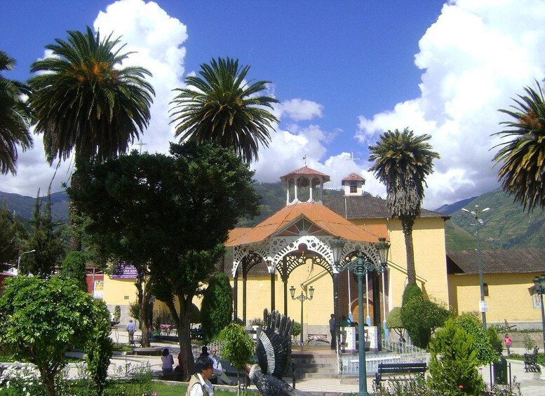Una iglesia con campanario, rodeada de palmeras y montañas al fondo. 2